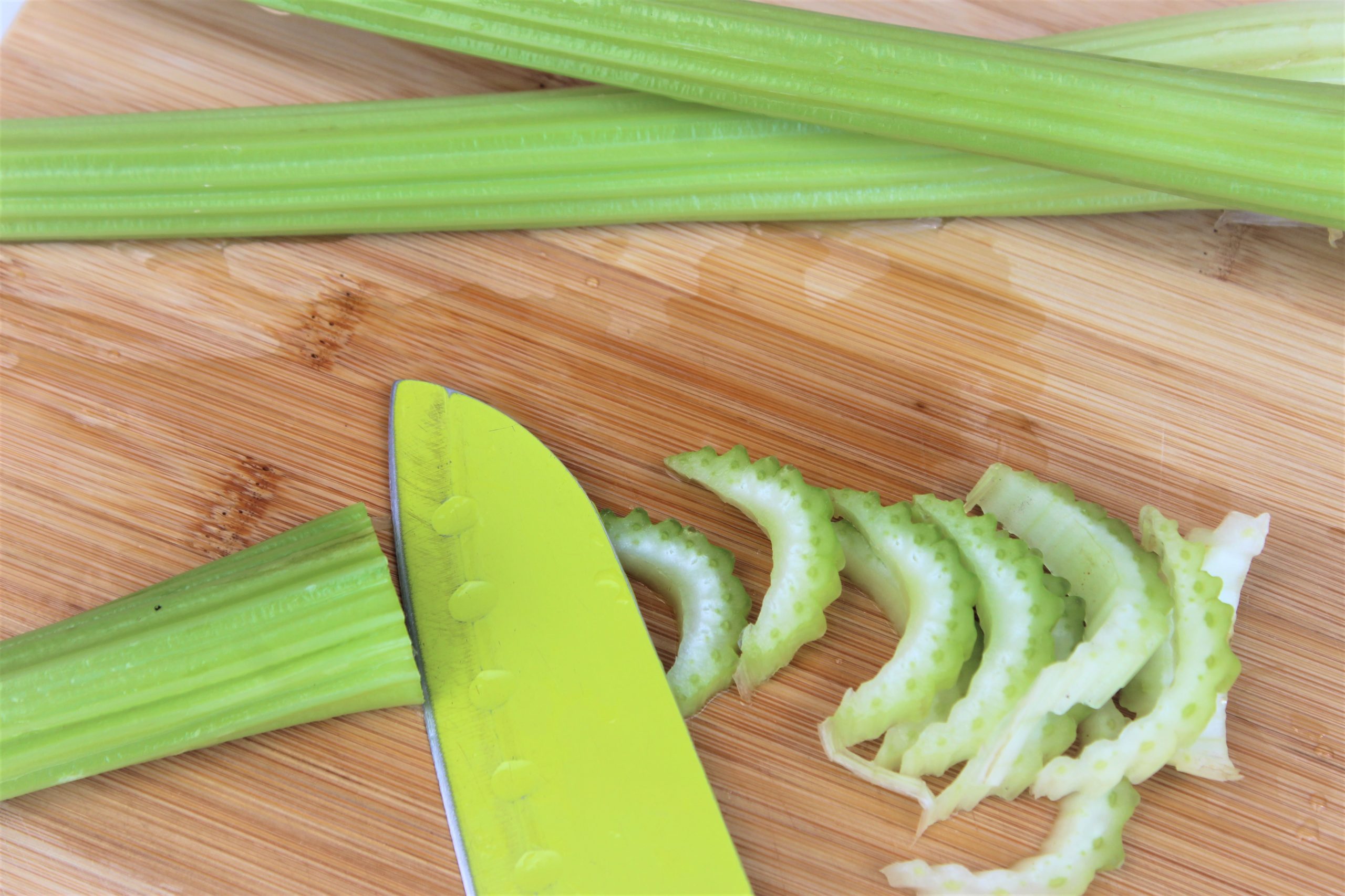 Thinly sliced celery on chopping board with a knife.