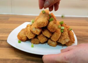 Plated fried tofu fingers on a plate being garnished with chopped spring onions.